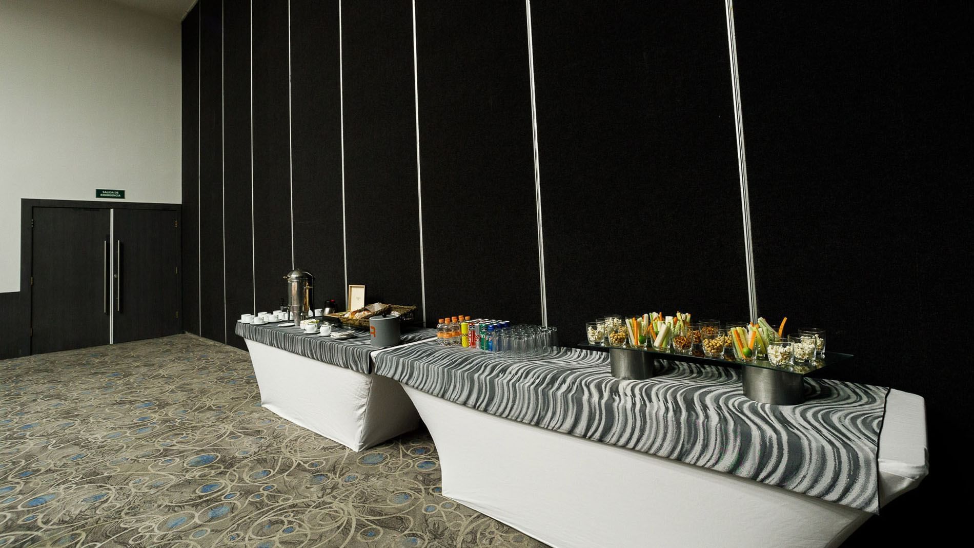 Milán catering station with snacks, coffee, and drinks against a black partition at Real Inn Tijuana