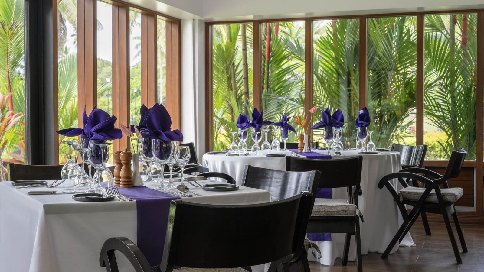 Dining tables with purple napkins by large windows under a white ceiling in Talei Restaurant at The Naviti Resort - Fiji