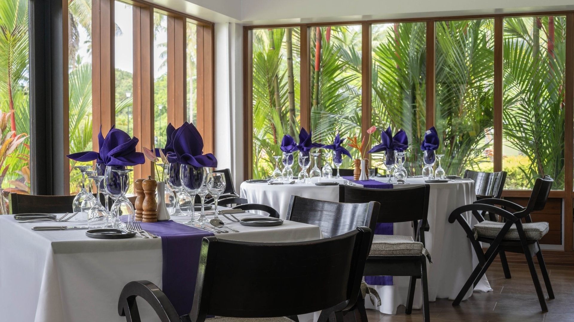 Dining tables with purple napkins by large windows under a white ceiling in Talei Restaurant at The Naviti Resort - Fiji