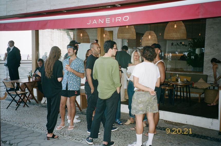 Grupo de pessoas em pé comversando no bar Janeiro Hotel em frente à praia