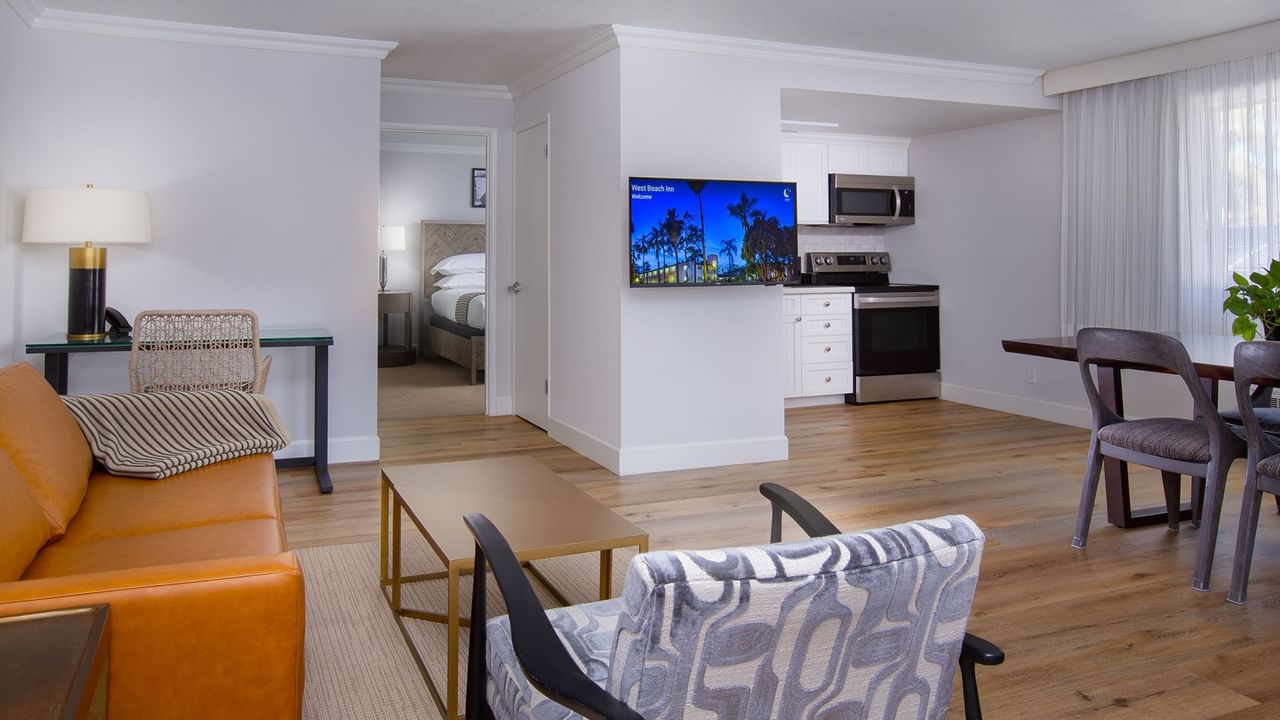 Living room with couch, armchair, coffee table, flat-screen TV, kitchen with microwave, and dining area.