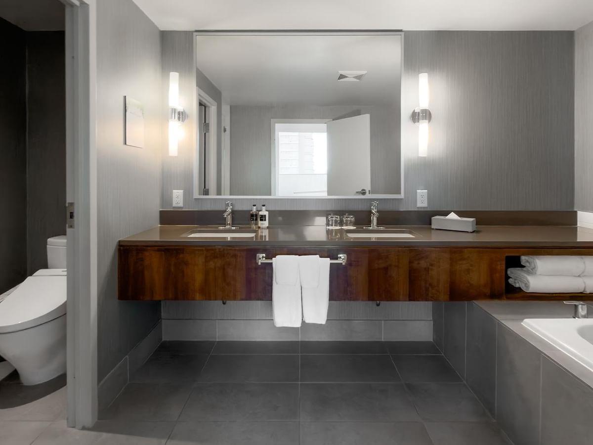 Modern bathroom with large mirror, double sinks, bathtub, and toilet.