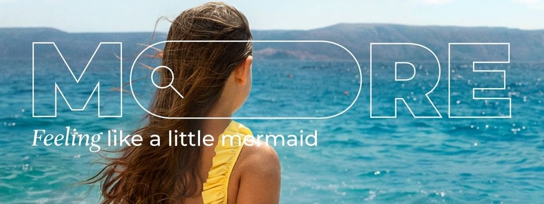 Woman in yellow swimsuit sitting on sandy beach gazing at turquoise ocean under clear blue sky.