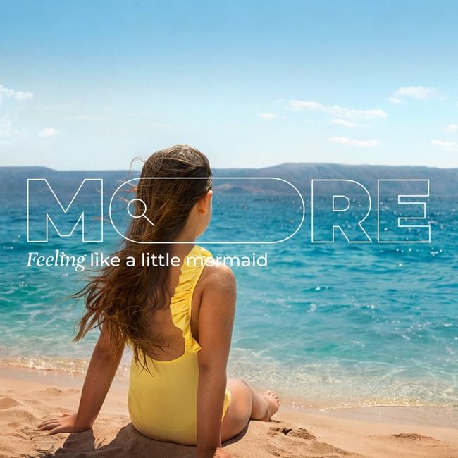 Woman in yellow swimsuit sitting on sandy beach gazing at turquoise ocean under clear blue sky.