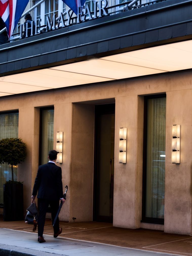 Man with umbrella walking into the main entrance of The May Fair Hotel