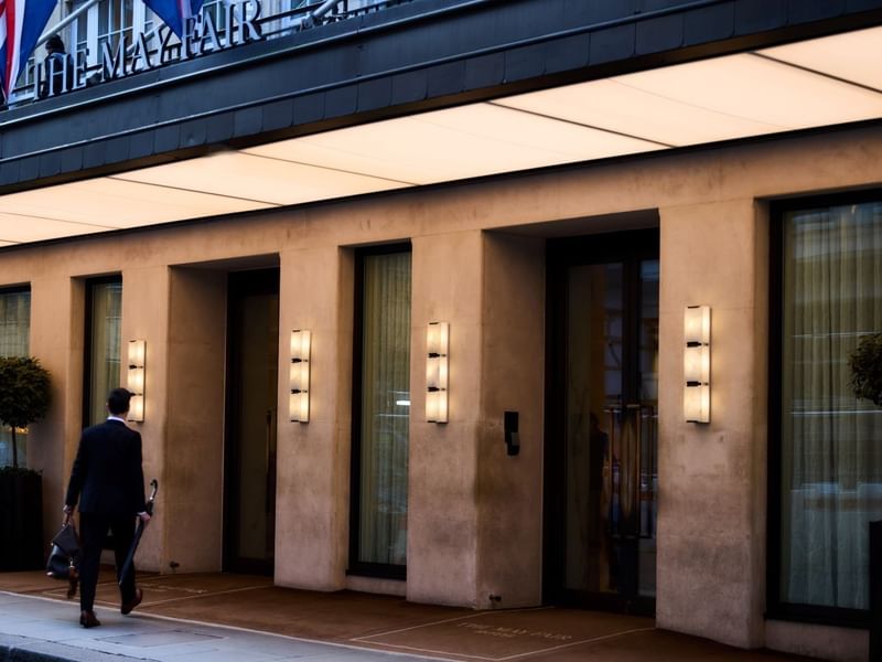 Man with umbrella walking into the main entrance of The May Fair Hotel