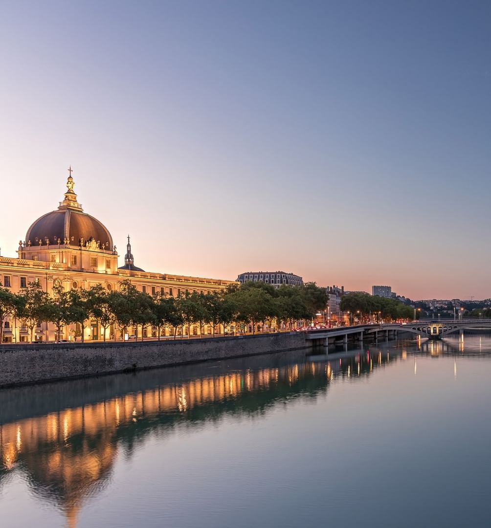 Illuminated historic dome building by a tranquil river at dusk near Warwick Reine Astrid - Lyon
