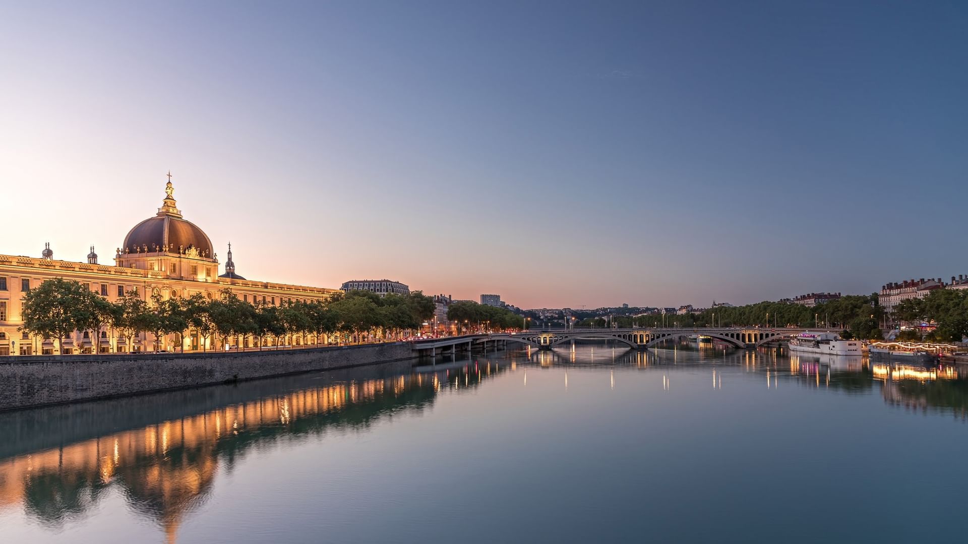 Illuminated historic dome building by a tranquil river at dusk near Warwick Reine Astrid - Lyon