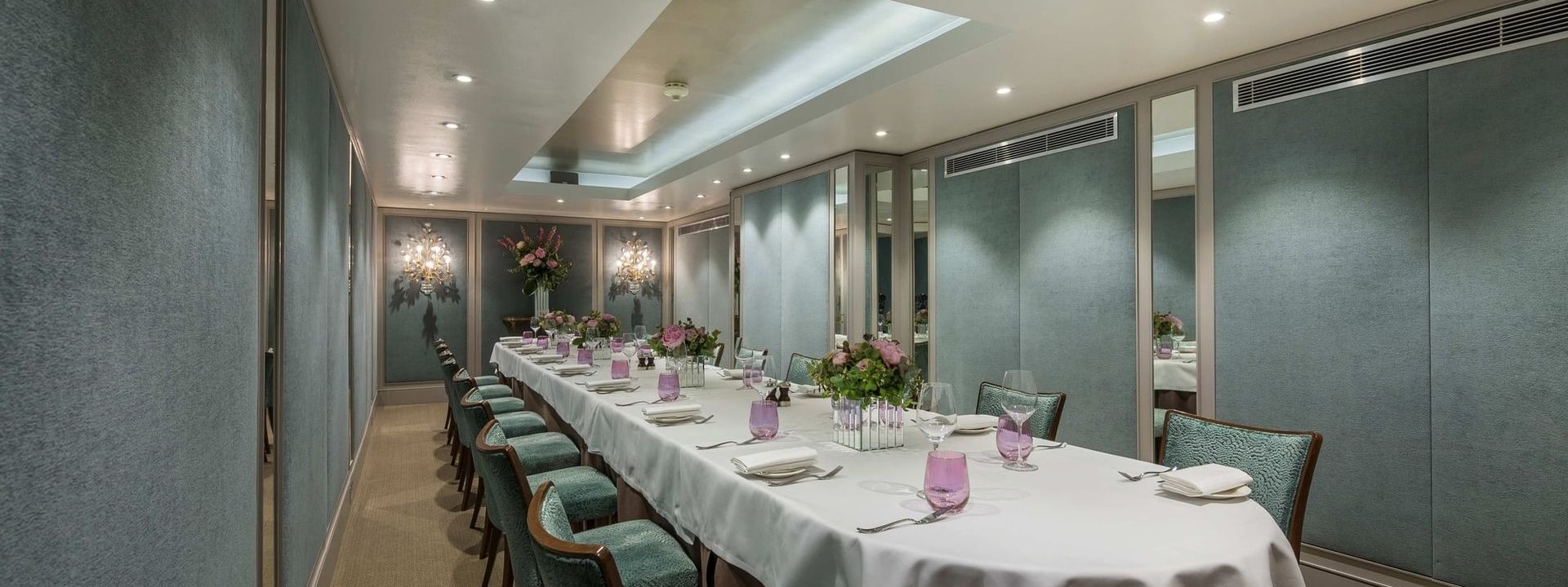 Long dining table with teal chairs by paneled walls under a recessed ceiling in Cadogan Suite at Warwick Hotels & Resorts