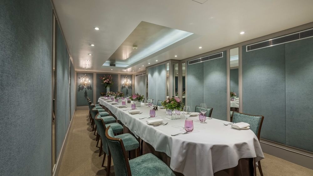 Long dining table with teal chairs by paneled walls under a recessed ceiling in Cadogan Suite at Warwick Hotels & Resorts