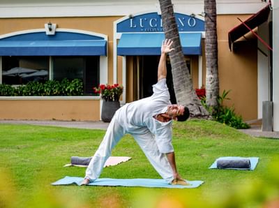 Persona con atuendo blanco practica yoga sobre una esterilla en un área de césped del Sunset Plaza Beach Resort, uno de los mejores hoteles con vistas a la playa en Puerto Vallarta