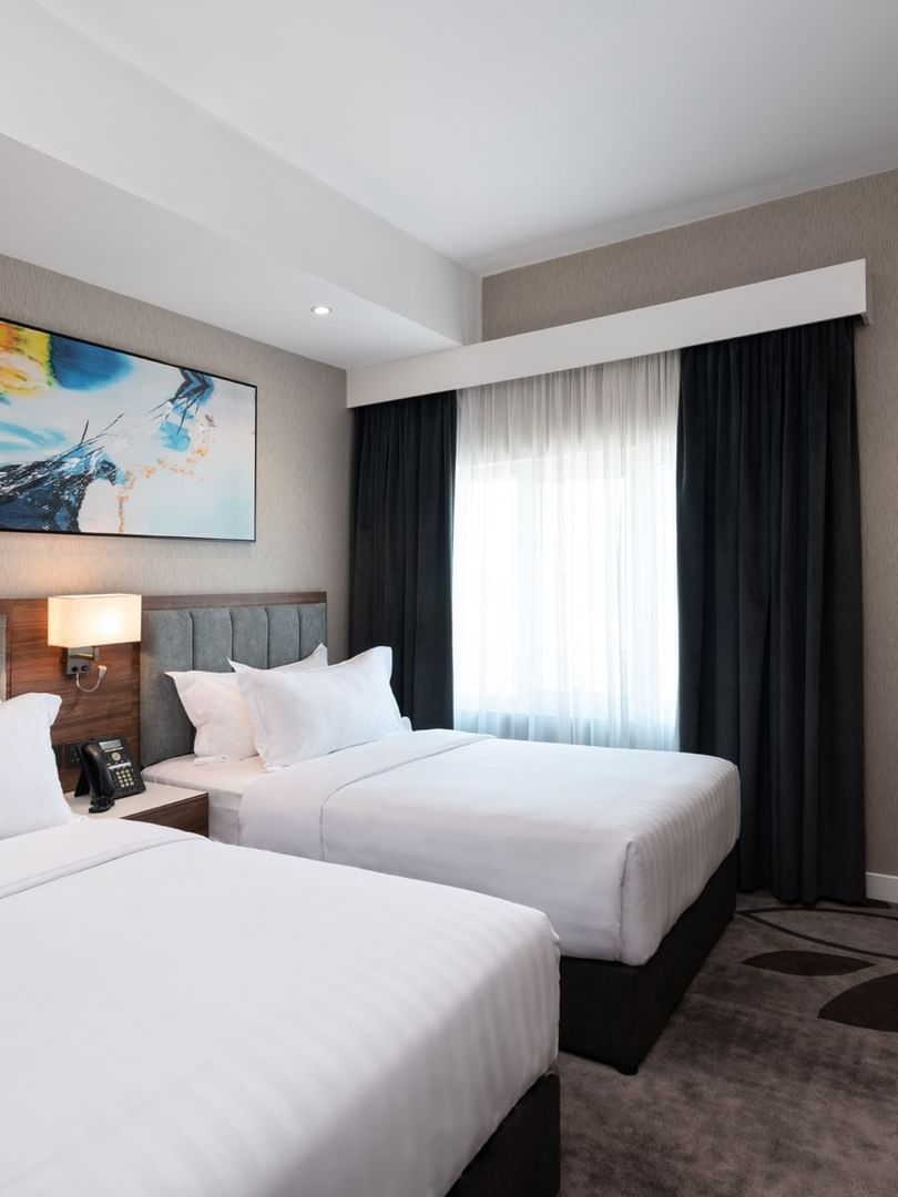 Twin beds with grey headboards under a vibrant abstract blue wall painting in Executive Room at Warwick Al Jubail City View 