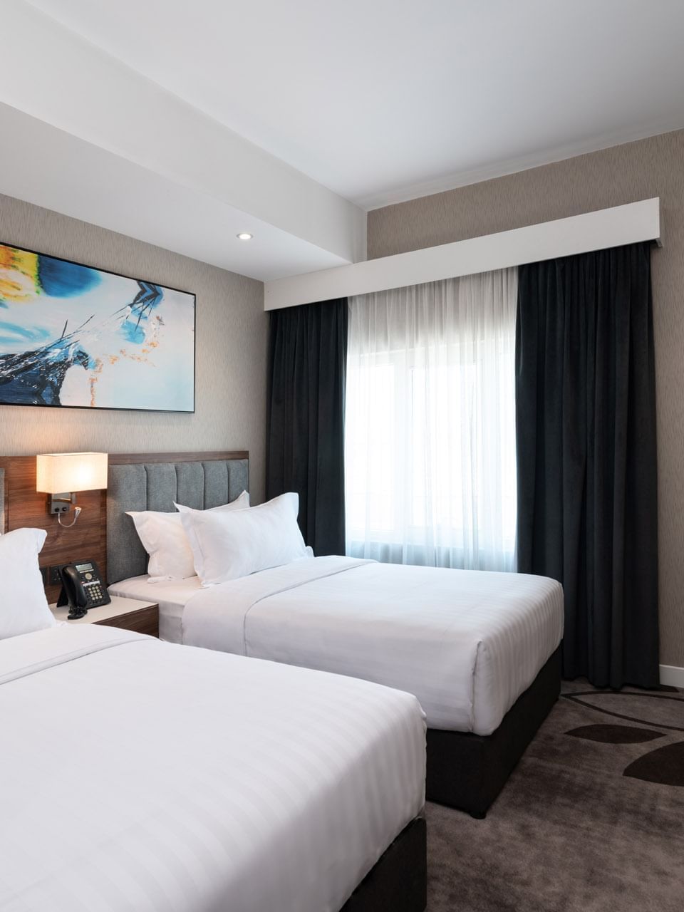 Twin beds with grey headboards under a vibrant abstract blue wall painting in Executive Room at Warwick Al Jubail City View 