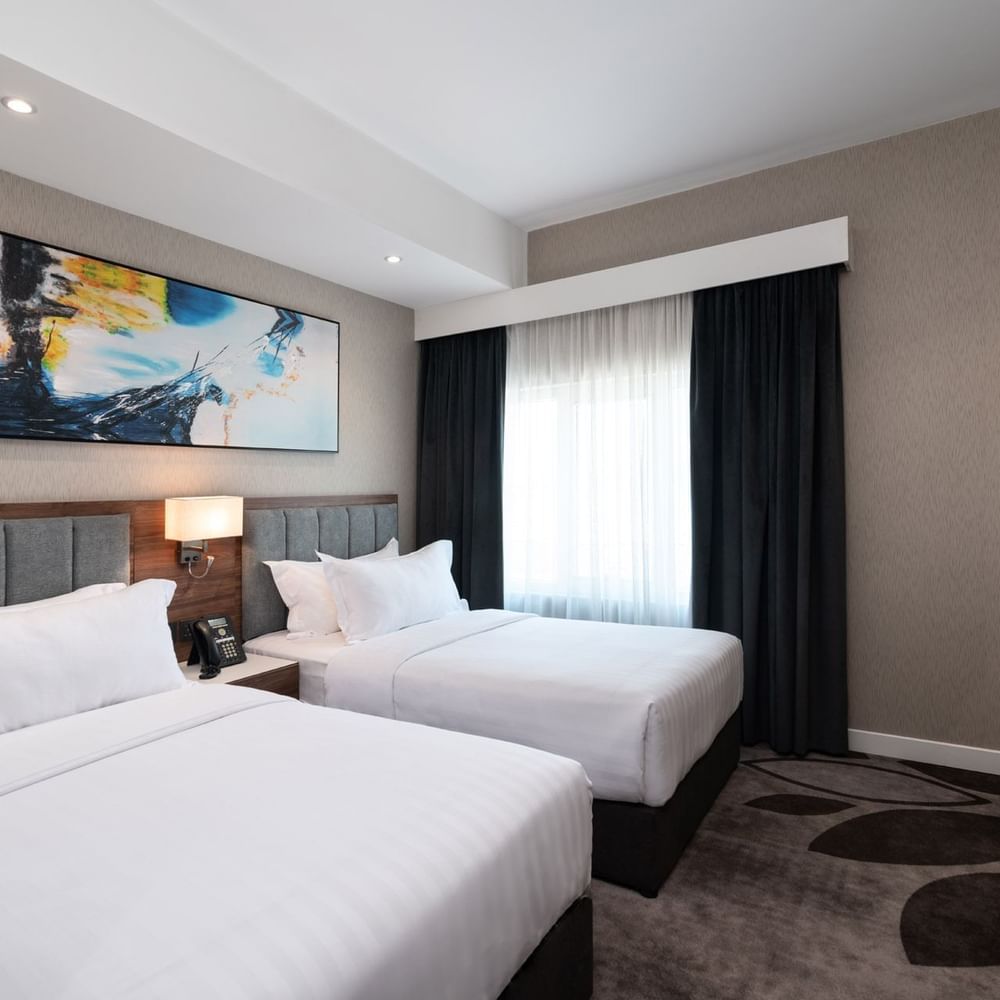 Twin beds with grey headboards under a vibrant abstract blue wall painting in Executive Room at Warwick Al Jubail City View 