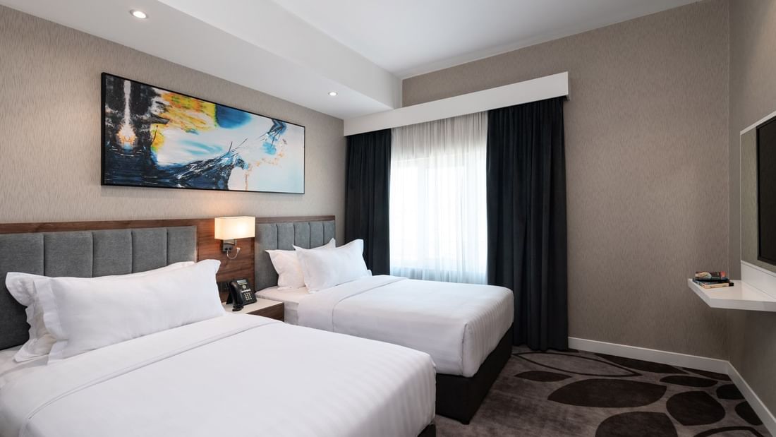Twin beds with grey headboards under a vibrant abstract blue wall painting in Executive Room at Warwick Al Jubail City View 
