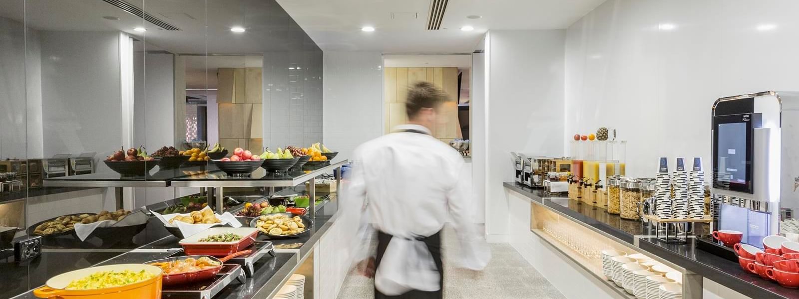 Waiter walking through the well-stocked kitchen with various food options in Grab & Go at Ibis Adelaide