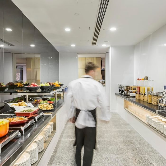 Waiter walking through the well-stocked kitchen with various food options in Grab & Go at Ibis Adelaide