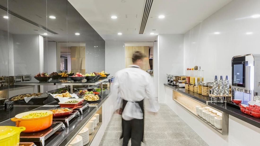 Waiter walking through the well-stocked kitchen with various food options in Grab & Go at Ibis Adelaide