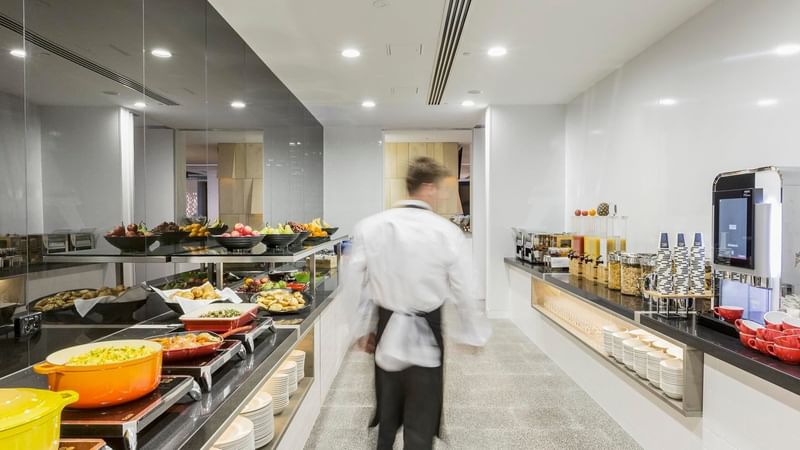 Waiter walking through the well-stocked kitchen with various food options in Grab & Go at Ibis Adelaide