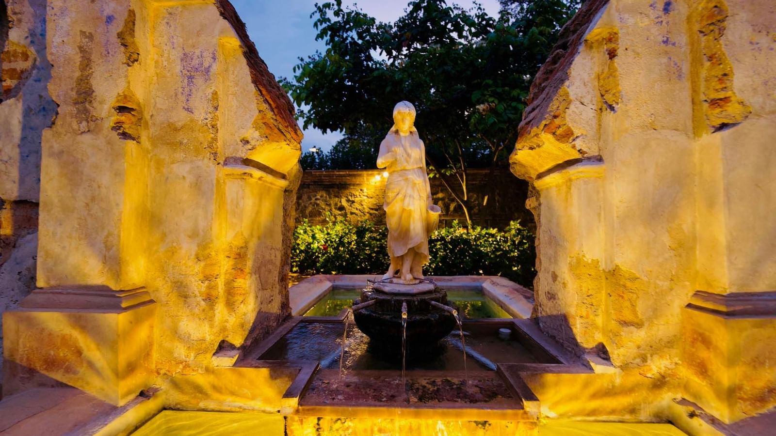Fuente y estatua encantadas bañadas en luz cálida, rodeadas de históricas ruinas de piedra en Casa Santo Domingo