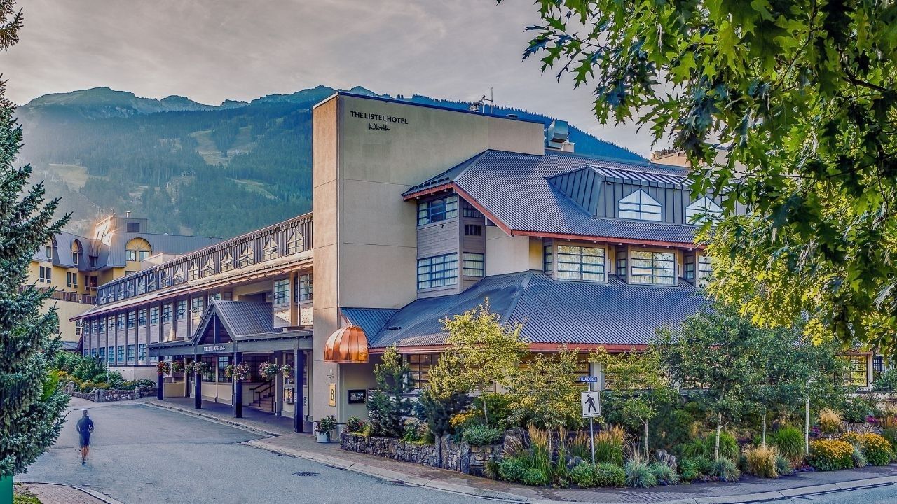 Exterior of The Listel Hotel Whistler with mountains in the background and a person jogging.