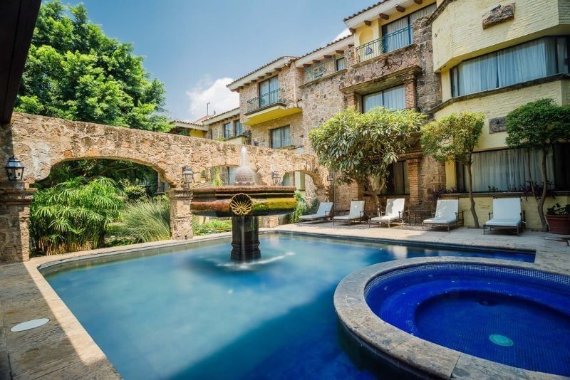 Stone fountain in a pool by lounge chairs under a leafy tree and stone arch at Camino Real Pedregal Mexico