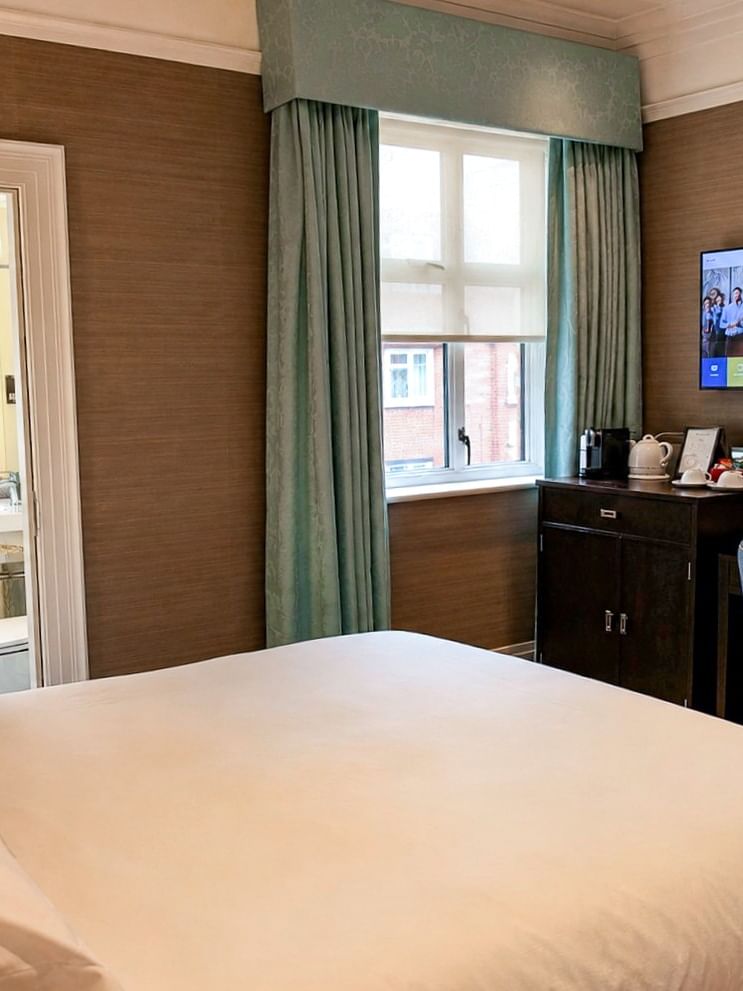 Teal curtains by a window and TV near an open door showing the white bathroom area at Warwick Hotels & Resorts