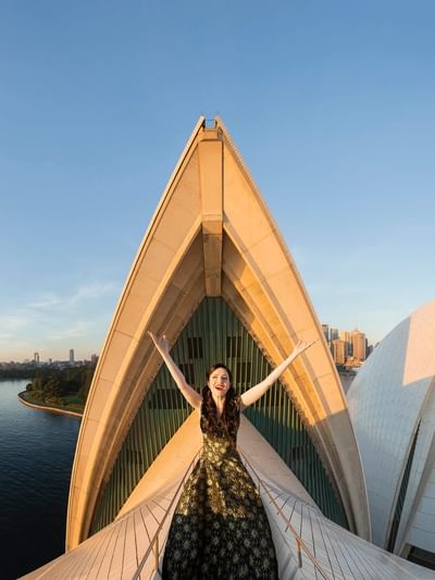 A woman stands on the edge of Sydney Opera House at sunrise for The Great Opera Hits.