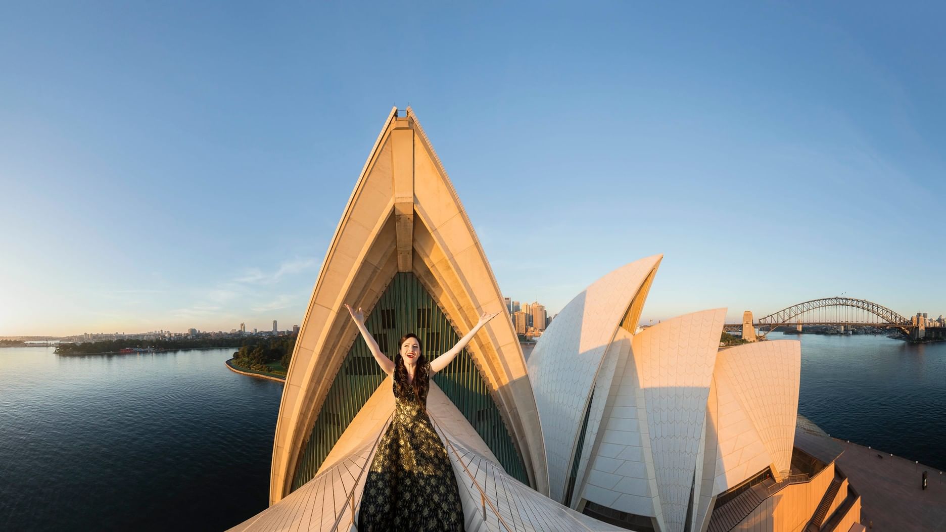 A woman stands on the edge of Sydney Opera House at sunrise for The Great Opera Hits.