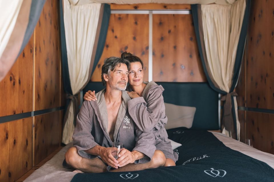 A couple in robes seated on a bed in Orjola spa at Liebes Rot