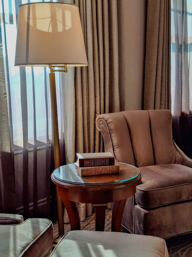 Two classic books on a glass table by a velvet armchair under a tall floor lamp in Deluxe King at Warwick Melrose Dallas