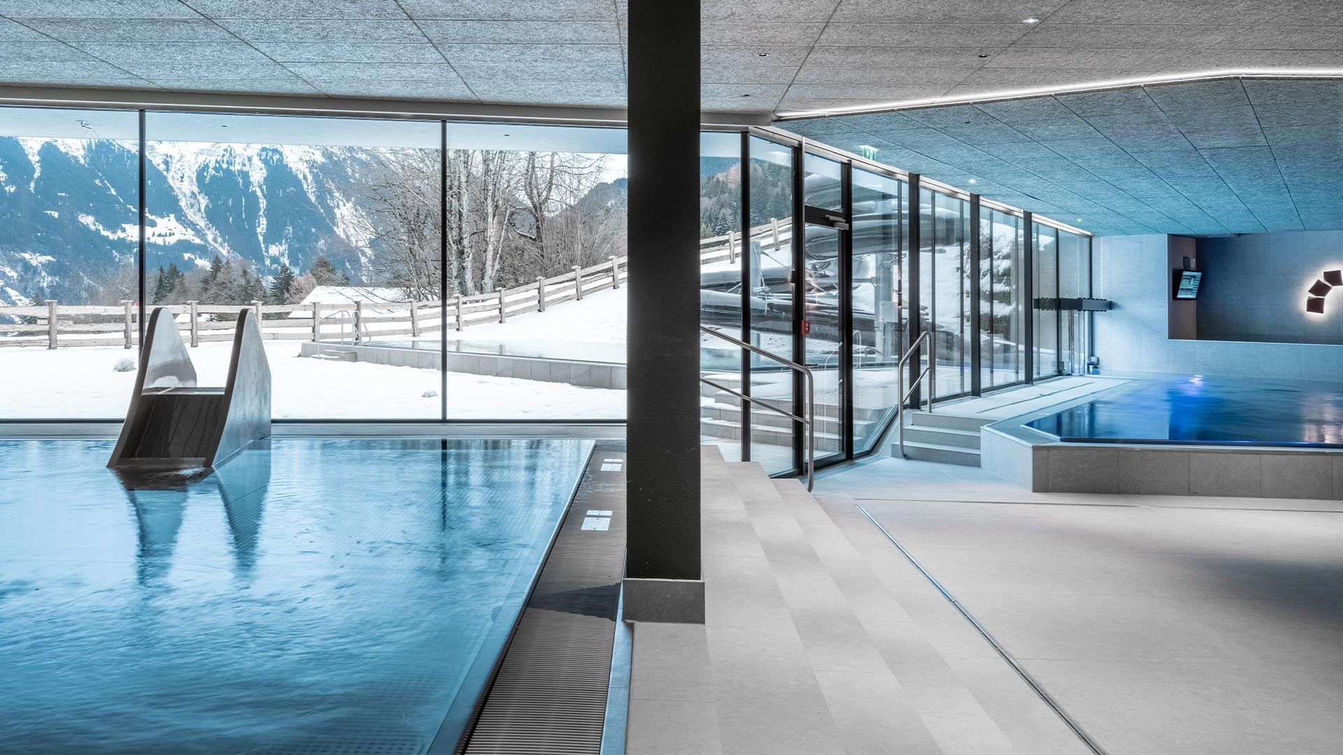 Indoor pool with windows overlooking snowy mountains at Falkensteiner Hotel Montafon