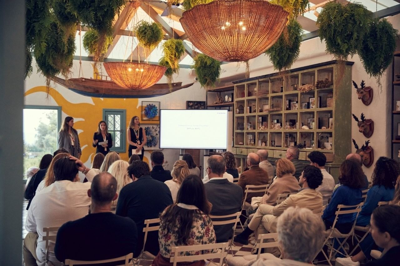 Indoor presentation with three women speaking to a seated audience, surrounded by hanging plants at Marbella Club