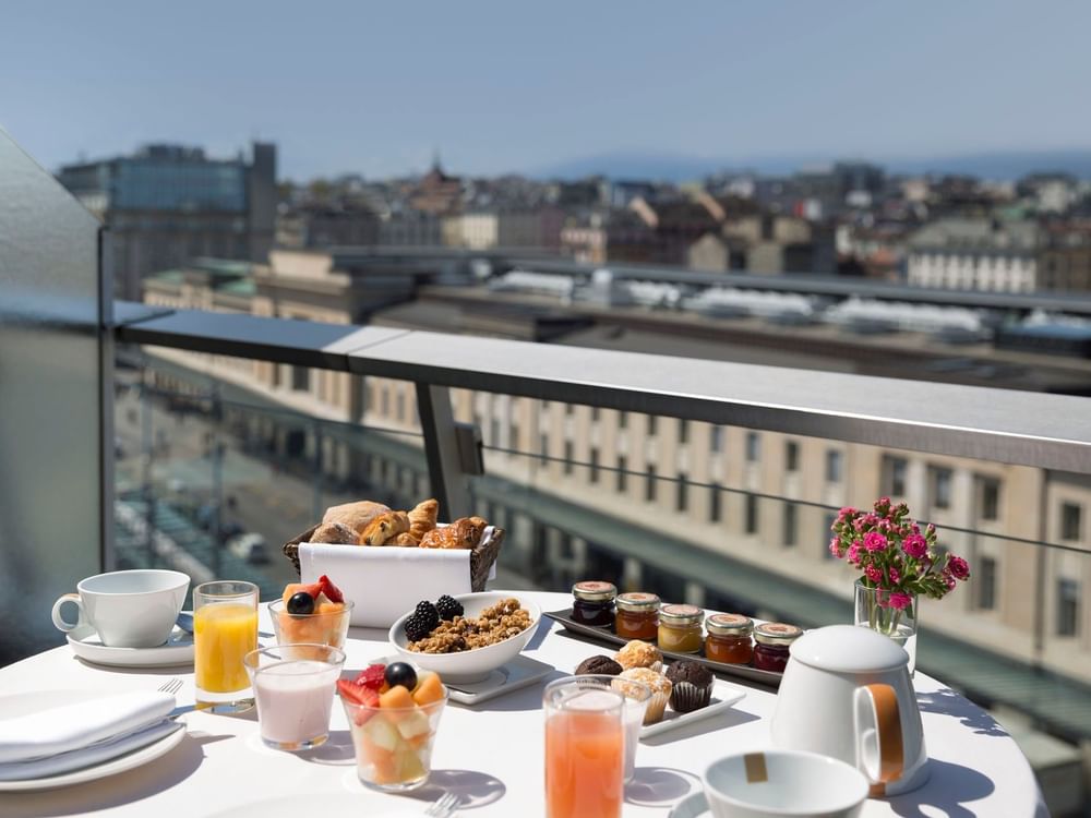 Fresh breakfast tray by a vase of pink flowers on a table in Penthouse Terrace Room at Warwick Geneva