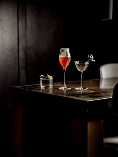 Three elegantly presented cocktails on a dark wood table served at The Kitchens