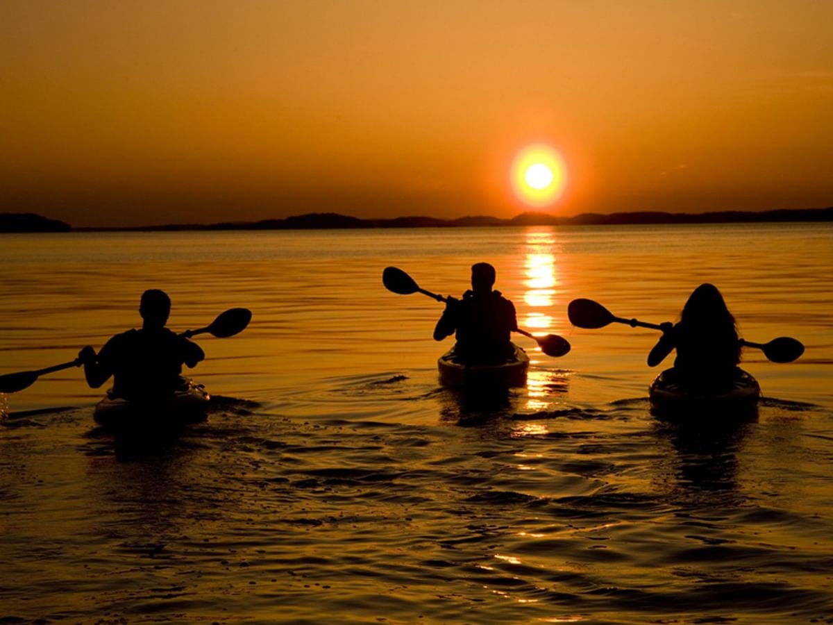 Three kayakers paddling on a lake under a glowing orange sun at Lake Ouachita State Park near Arlington Resort Hotel & Spa