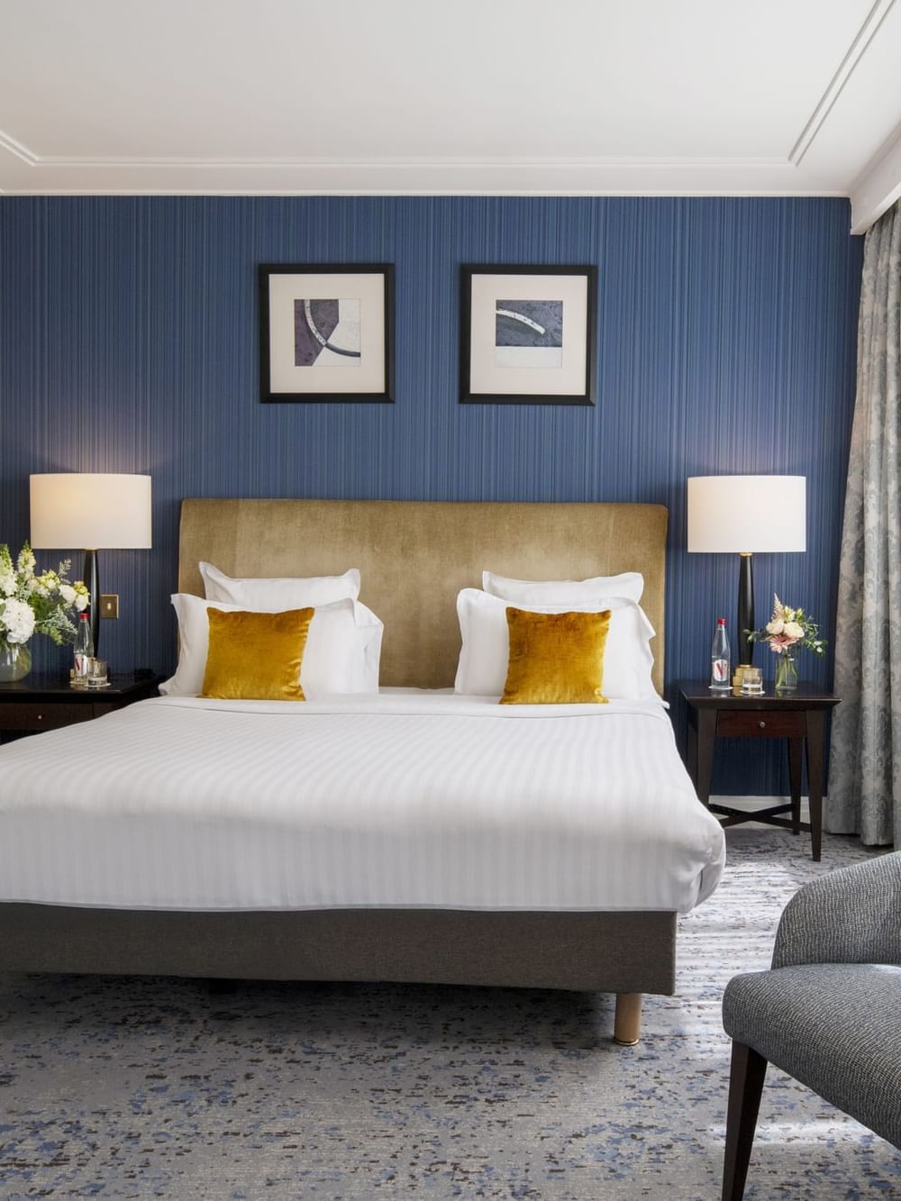 Grey armchair by a bed with a gold headboard under a blue textured wall in Deluxe Room at Warwick Paris Champs Elysées