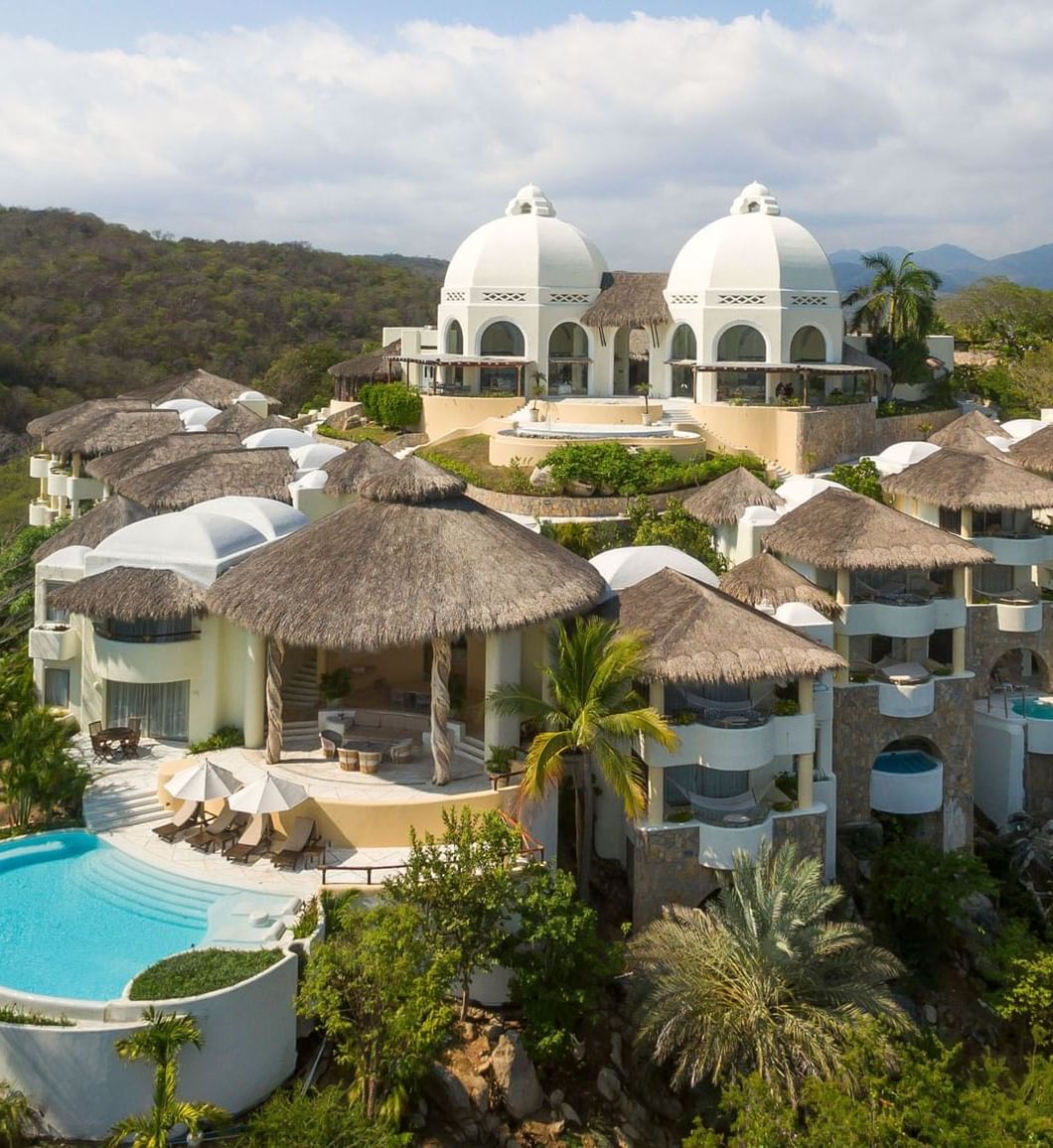 Aerial view of Quinta Real Huatulco featuring white domes by a pool surrounding thatched roofs at Tangolunda Bay