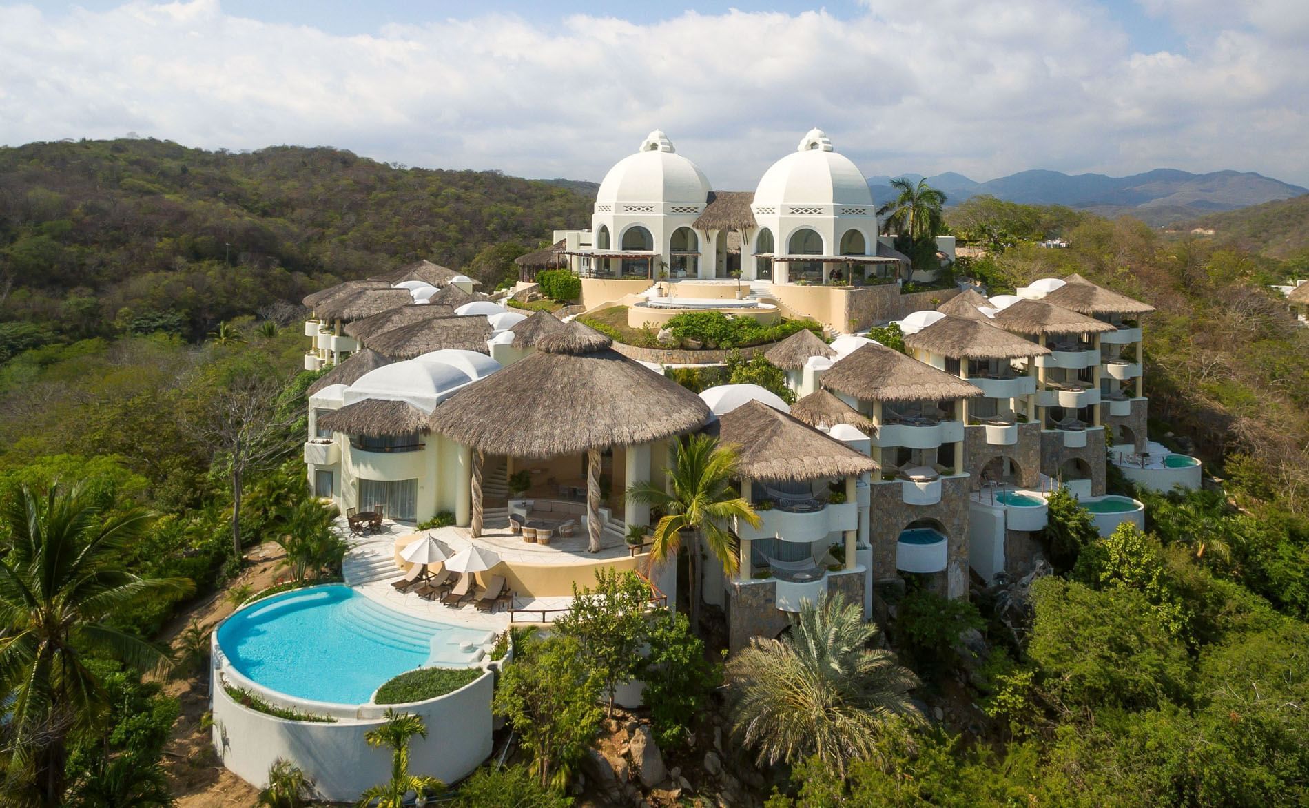 Aerial view of Quinta Real Huatulco featuring white domes by a pool surrounding thatched roofs at Tangolunda Bay