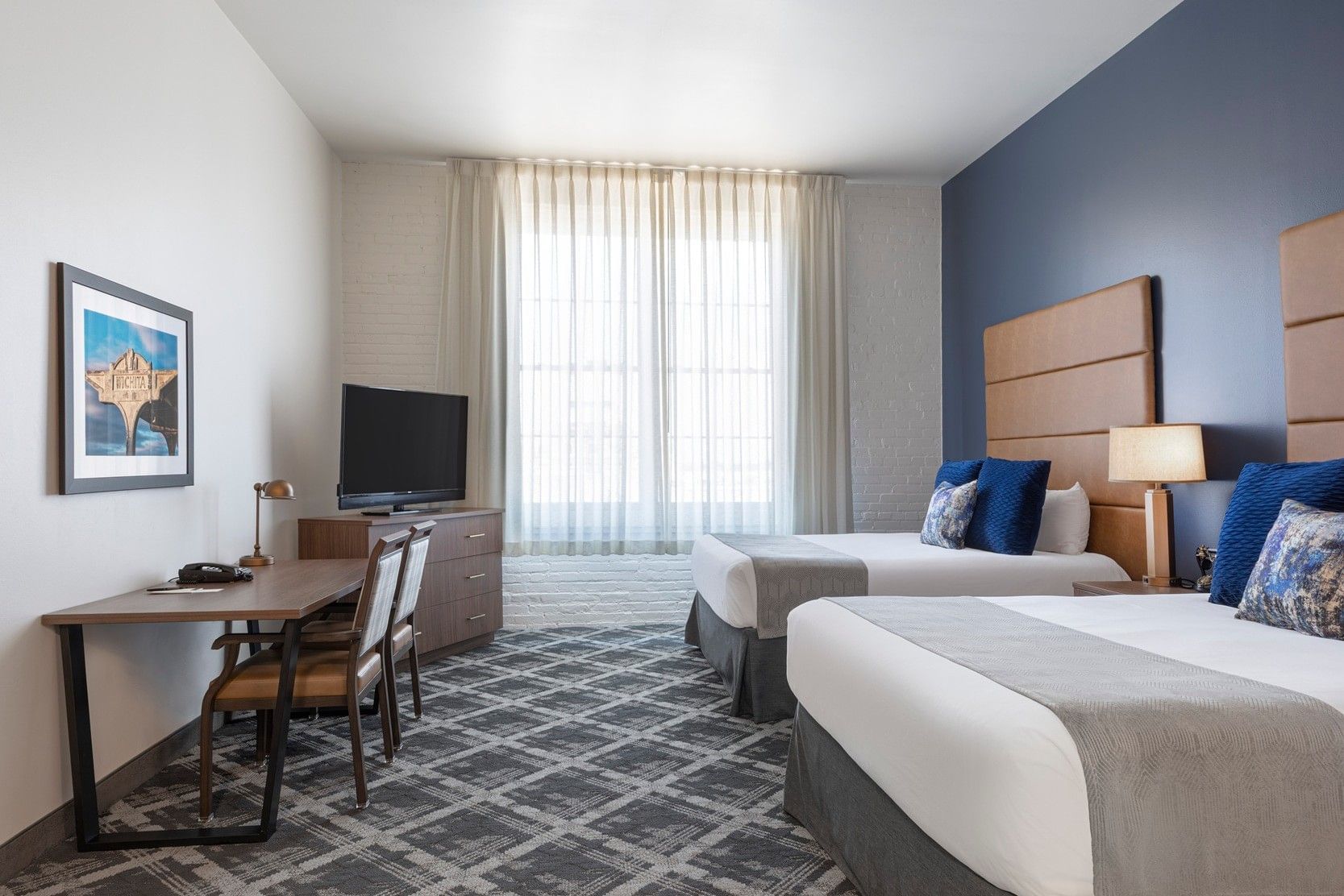 A hotel room with two beds, a desk, and a TV.