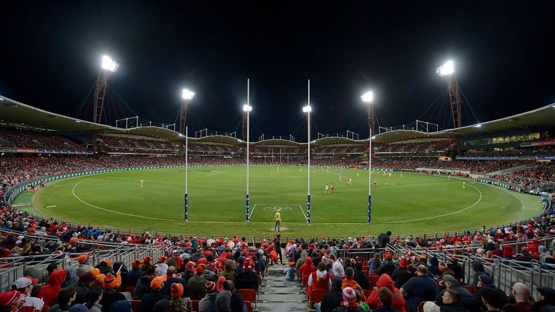 Nighttime stadium filled with spectators watching a sports game on a large green field with white lines.