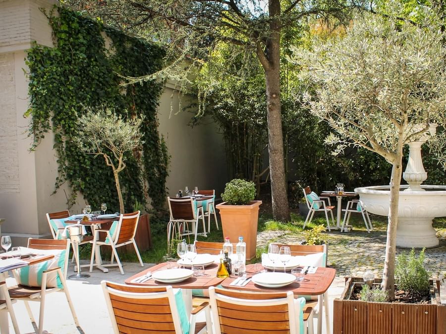 Hidden garden terrace dining area set with white plates & glassware and white stone fountain at Hotel Barsey by Warwick