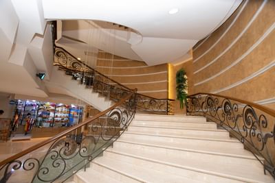 Staircase with ornate iron railing, leading to a curved upper level, surrounded by stylish golden walls at Dann Carlton Cali