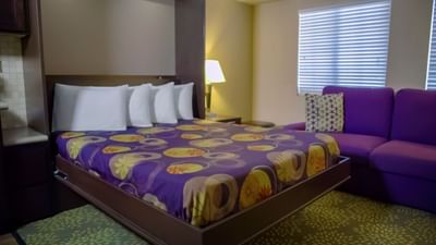 Guest room with purple patterned bedding, white pillows, purple sofa, and kitchenette at London Bridge Resort