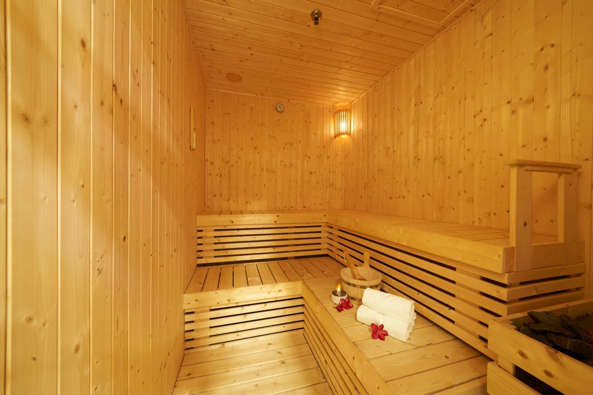 Warm wooden sauna with benches, soft towels, a bucket, and candlelight for a relaxing ambience at Orchard Grand Court