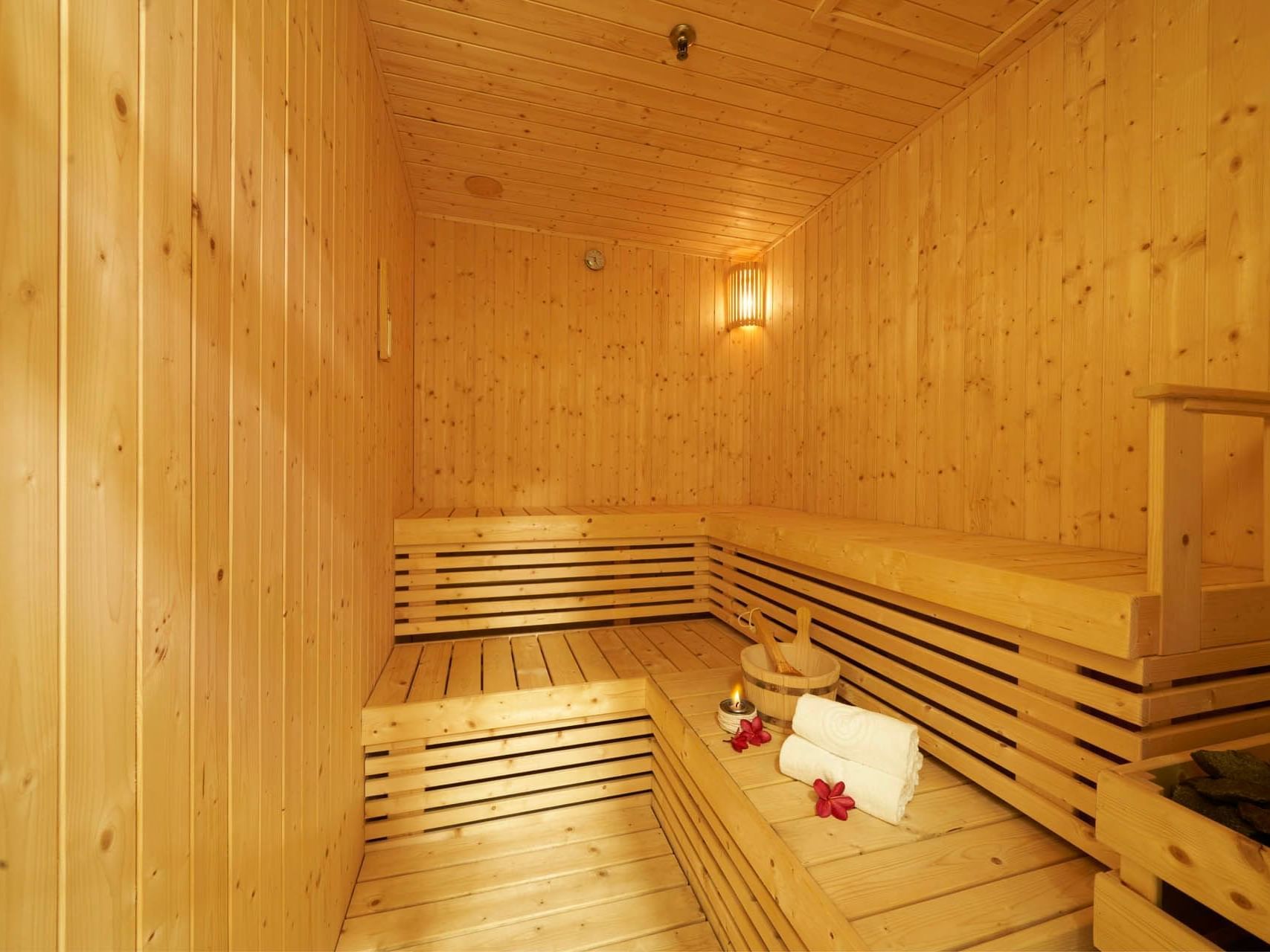 Warm wooden sauna with benches, soft towels, a bucket, and candlelight for a relaxing ambience at Orchard Grand Court