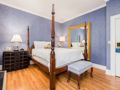 Four-poster bed with white linens by a striped bench, under a gilded mirror near a wooden dresser at Simsbury 1820 House