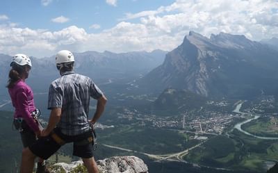 Two climbers admiring a mountain view, overlooking a lush valley and a winding river near Blackstone Mountain Lodge
