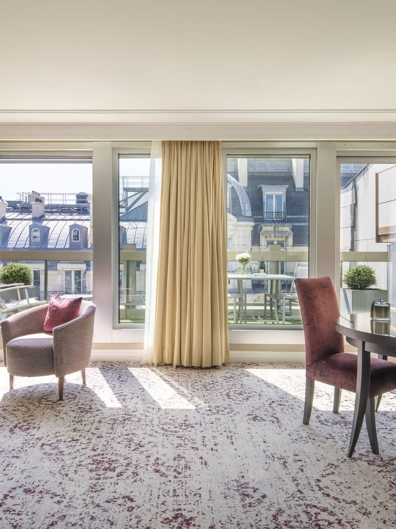 Purple chairs surrounding a round table by an chair under windows in The Montaigne Suite at Warwick Paris Champs Elysées