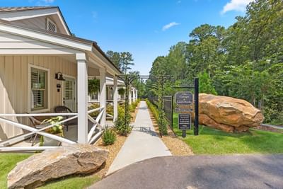Welcoming pathway to Cottages at Laurel Brooke, lined with lush greenery and large rocks on a sunny day
